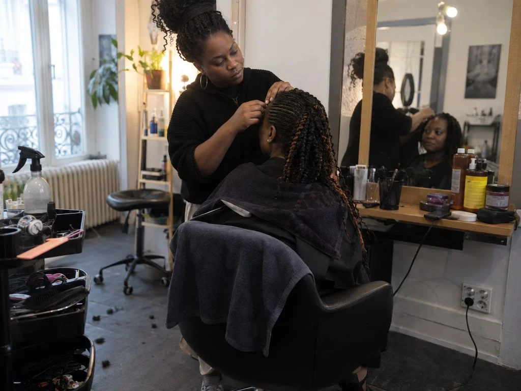 Coiffeuse desserrant des tresses à la lisière d'une cliente dans un salon