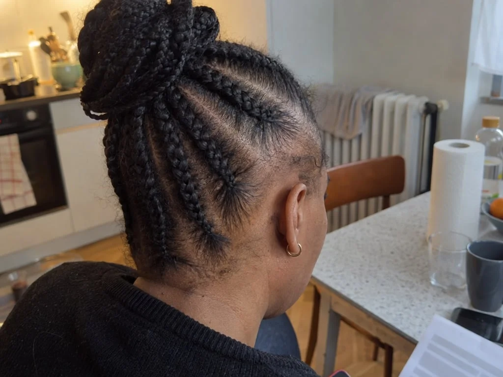 Femme vue de dos portant des tresses serrées ramenées en chignon, avec une lisière clairsemée aux tempes