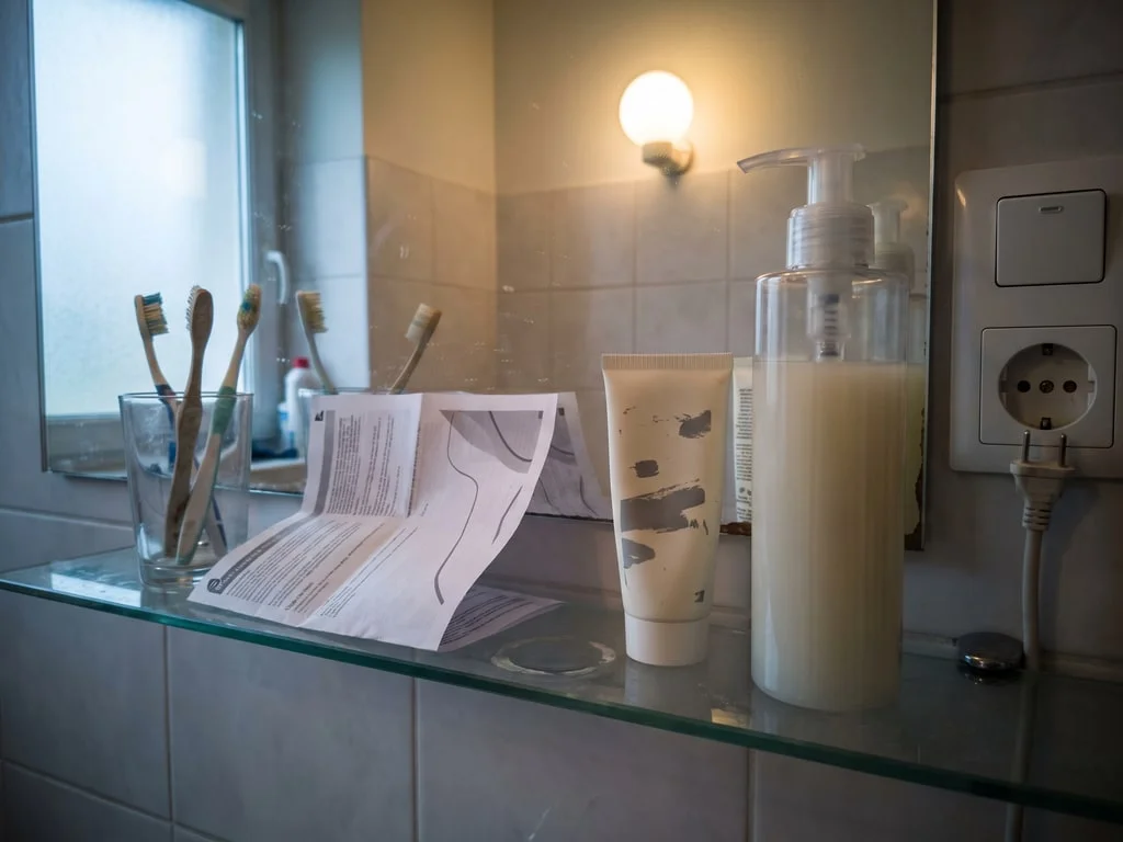 Un petit tube de crème et un flacon-pompe nettement plus grand posés côte à côte sur l'étagère d'une salle de bain, une notice dépliée derrière