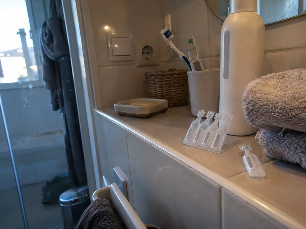 Dosettes de sérum physiologique près du lavabo : la recommandation cite le sérum physiologique et le shampooing doux comme deux options équivalentes pour le nettoyage précoce